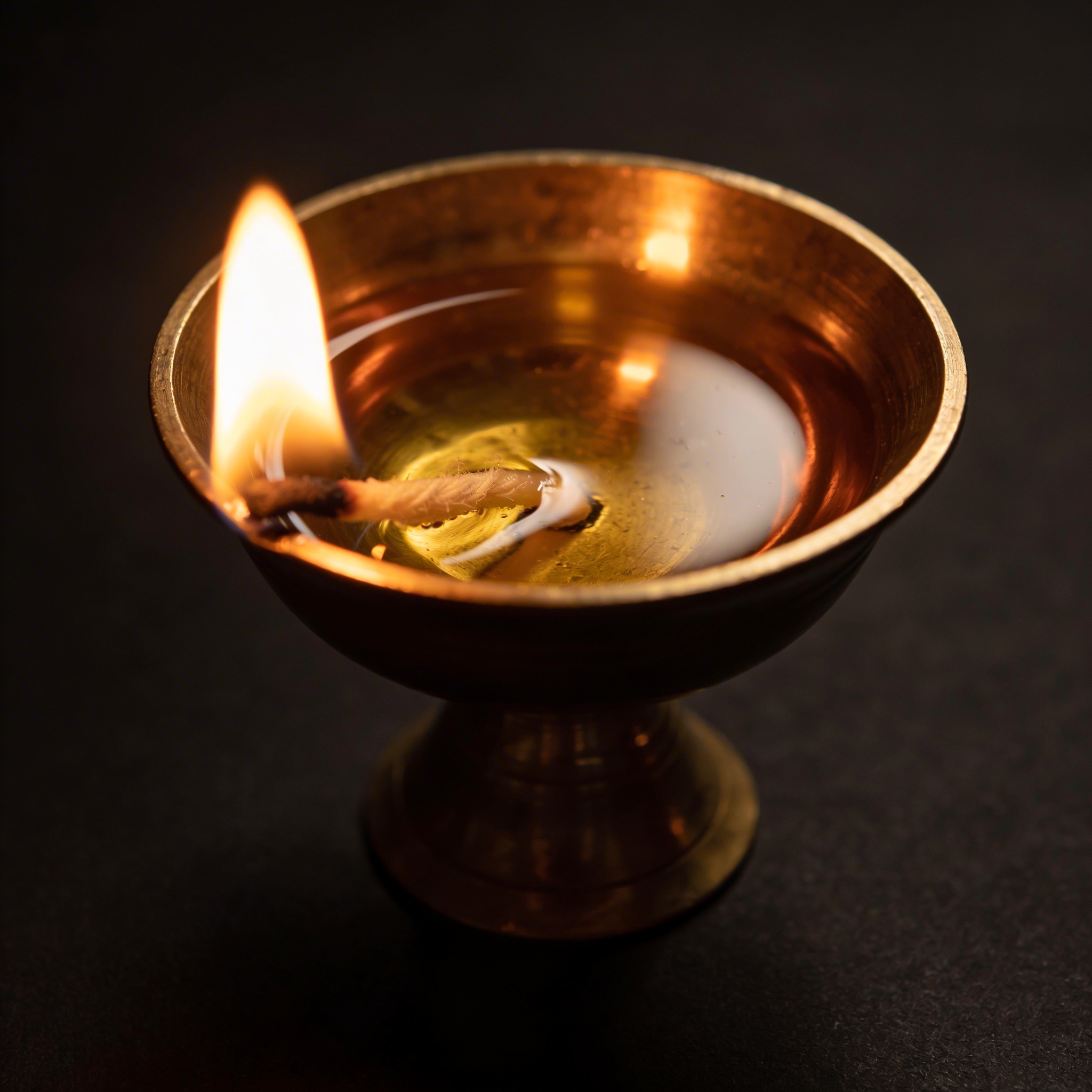 A single brass diya with a bright warm flame glowing in soft darkness, ghee-soaked cotton wick visible